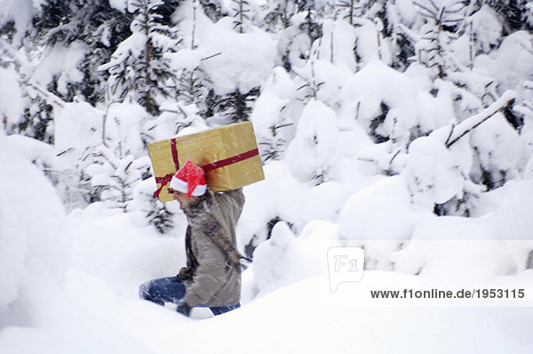 Junger Mann  der im Schnee läuft und ein Geschenk trägt.
