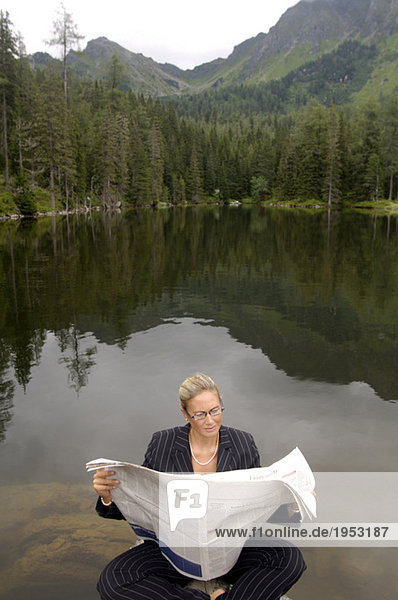 Businesswoman reading newspaper at lake
