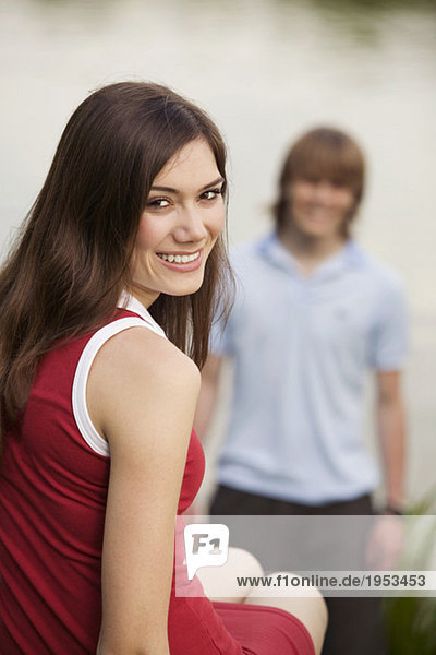 Junge Frau lächelt mit jungem Mann im Hintergrund
