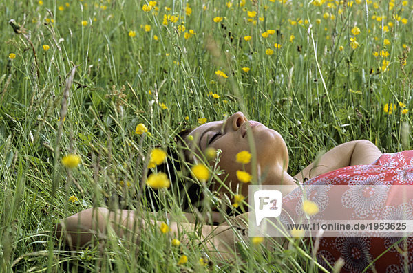 Junge Frau auf Gras liegend mit Händen hinter dem Kopf