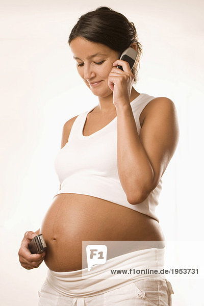 Pregnant woman holding cup on belly and ear