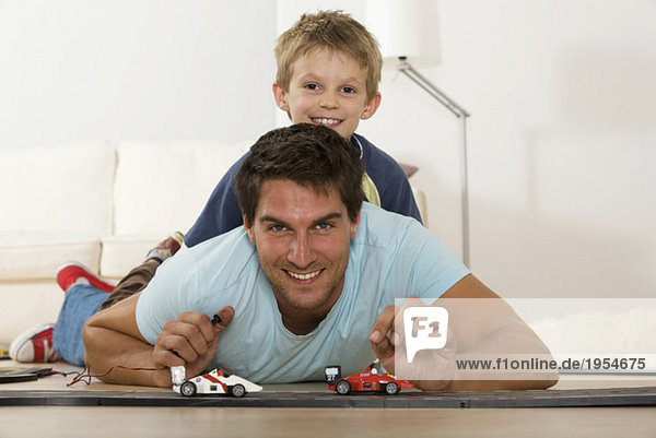 Father and son (6-7) playing with toy cars  smiling  portrait