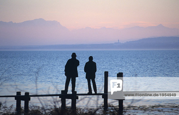 Silhouette of man and women standing on boardwalk  rear view  Ammersee  Bavaria  Germany