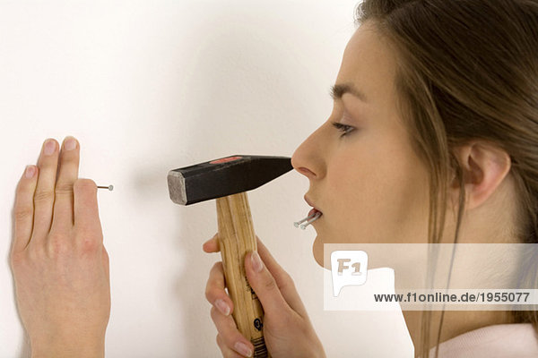Woman hammering nail into wall  close-up  profile