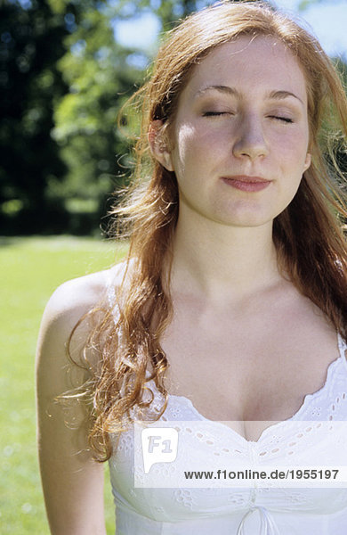 Junge Frau in weißem Kleid im Garten stehend  Augen geschlossen  Nahaufnahme