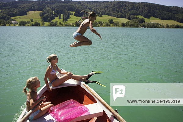 Mädchen (8-15) auf dem Boot sitzend,  eine springt im Wasser,  Seitenansicht