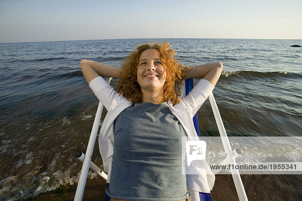Junge Frau entspannt sich im Liegestuhl am Strand  lächelnd  Nahaufnahme