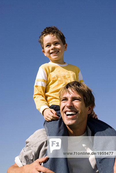 Junge (4-7) auf Vaters Schultern sitzend  lächelnd  Nahaufnahme