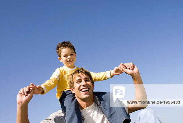 Boy (4-7) sitting on fathers shoulders  smiling  portrait
