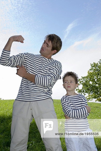 Father and son (4-7) flexing muscles  standing in park