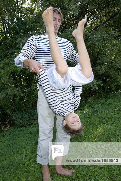 Father playing with son (4-7) in park  holding upside down