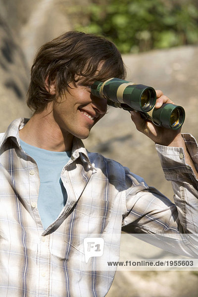 Young man looking through binoculars  smiling