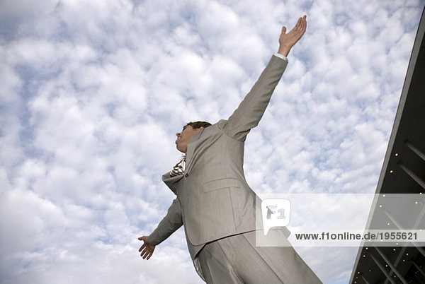 Businessman against cloudy sky  arms out  low angle view