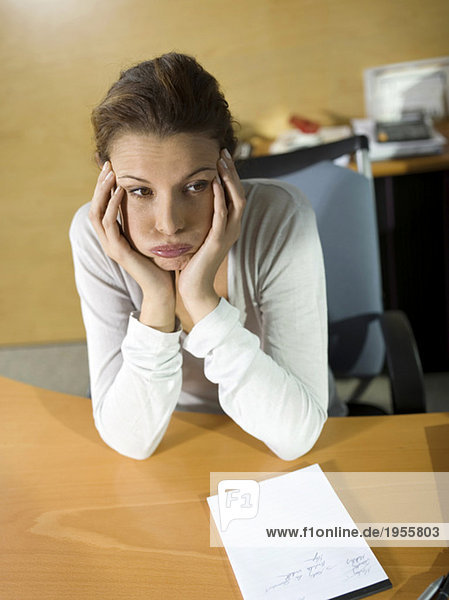 Müde Frau sitzt am Schreibtisch  Kopf in den Händen  Nahaufnahme
