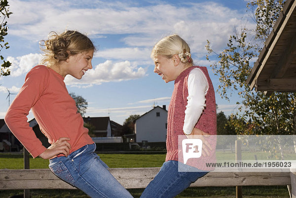 Zwei Mädchen (8-11) auf Holzgeländer  Hand auf Hüfte  Seitenansicht