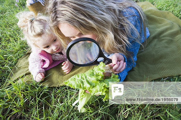 Mutter und Tochter beobachten Salatblatt durch Lupe
