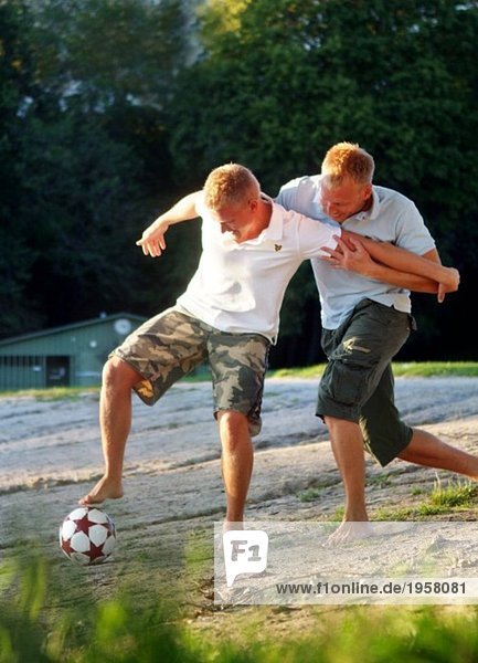 Two guys fighting over a football on a beach