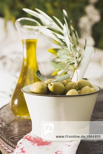 Grüne Oliven,  Olivenzweig und Olivenöl auf Tisch im Freien