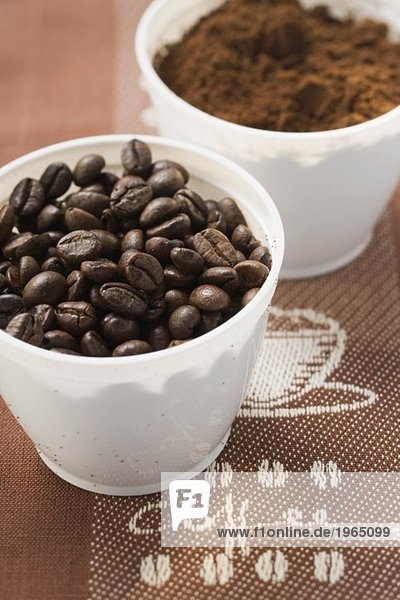 Kaffeebohnen und Kaffeepulver in zwei Bechern