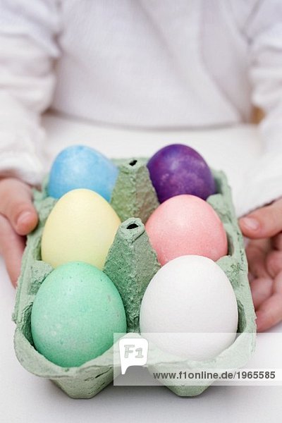 Kind hält Eierkarton mit gefärbten Eiern