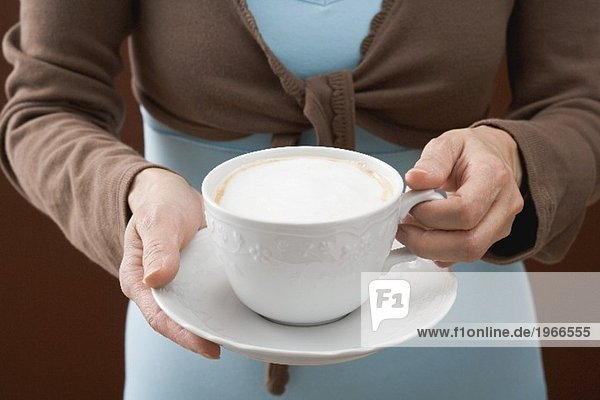 Frau hält Tasse Cappuccino
