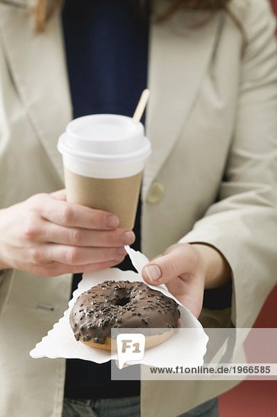 Frau hält Schokoladendoughnut und Kaffeebecher