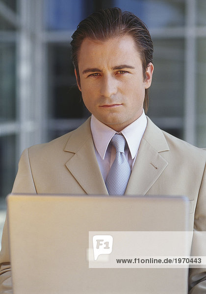 Manager steht mit Laptop vor Bürogebäude  Halbporträt