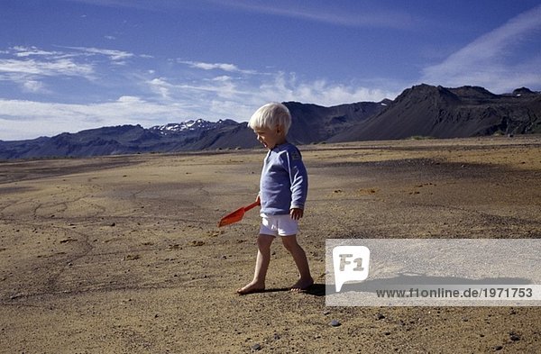 A little boy with a plastic spade in the sand at Snaefellsnes Iceland