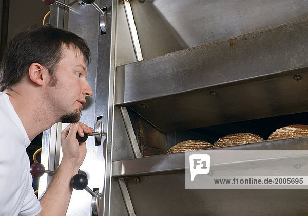 Bäckerei  Bäcker kontrolliert Brote im Backofen