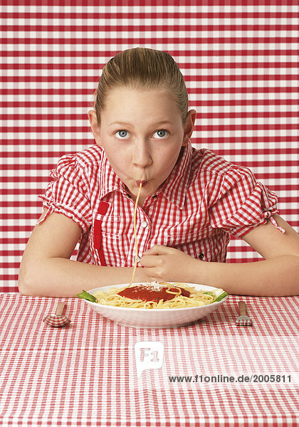Mädchen saugt einzelne Spaghetti von Teller