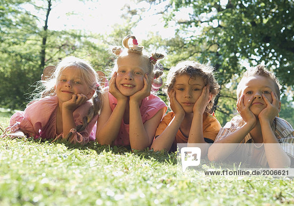 Vier Kinder liegen nebeneinander auf Wiese