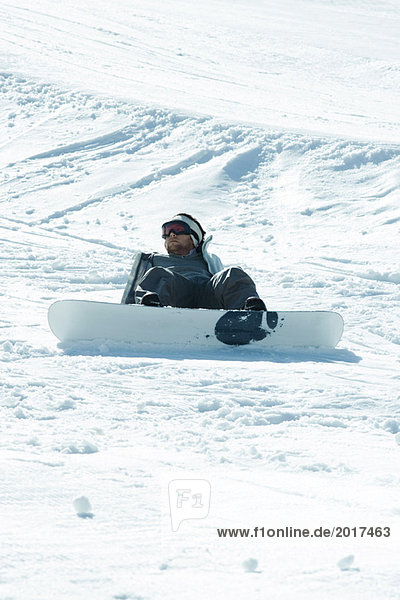 Junger Snowboarder auf dem Boden sitzend  gefallen