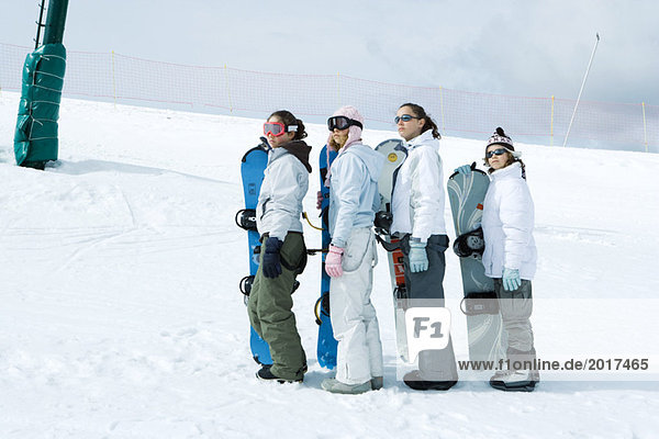 Four young snowboarders standing  lined up  looking up