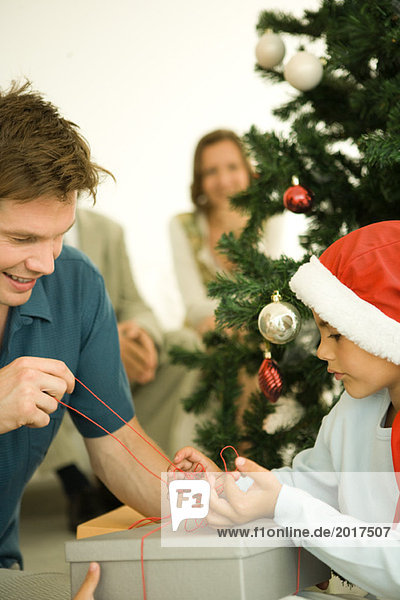 Father and son opening present together by Christmas tree