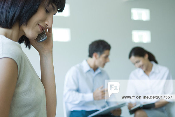 Young businesswoman using cell phone  colleagues working in background