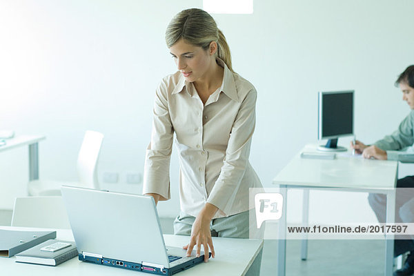Junge Geschäftsfrau am Schreibtisch stehend  mit Laptop