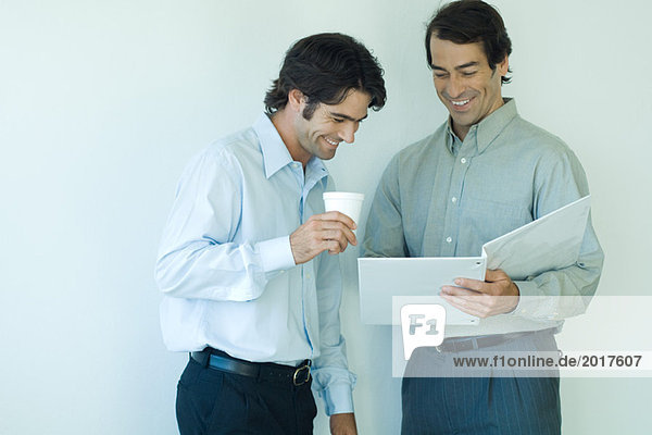 Zwei männliche Kollegen schauen sich gemeinsam die Akte an  lachend