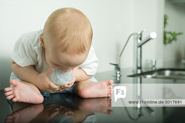 Baby sitzt auf der Küchentheke  hält die Flasche  schaut auf die Spiegelung herab