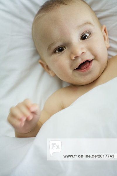 Baby in bed  under covers  smiling at camera