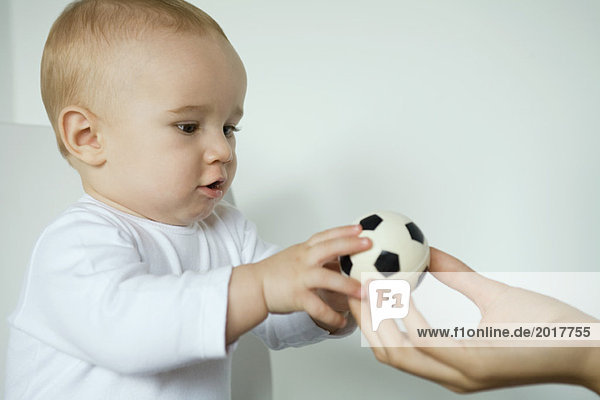 Baby nimmt Ball aus der Hand der Mutter  Nahaufnahme