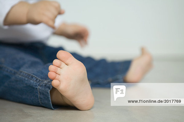 Baby in Jeans,  auf dem Boden sitzend,  niedrige Sektion,  Fokus auf Vordergrund