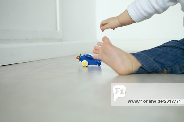 Baby auf dem Boden sitzend  nach dem Spielzeugflugzeug greifend  niedrige Sektion