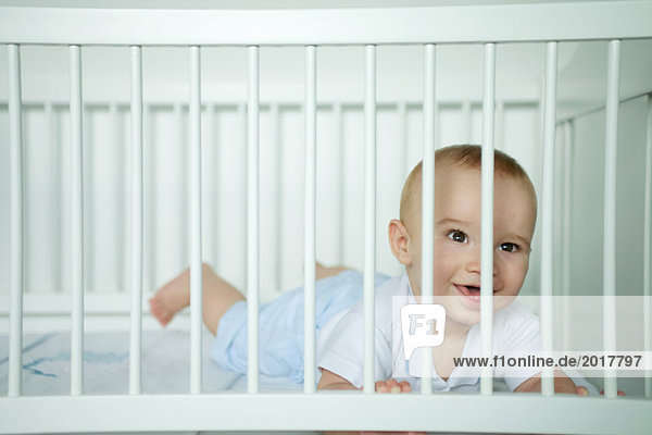 Baby auf dem Bauch liegend  durch Gitterstäbe schauend  lächelnd