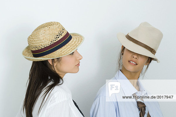Zwei junge Freundinnen mit Hüten und Krawatten  die sich anschauen  die Augen bedeckt.