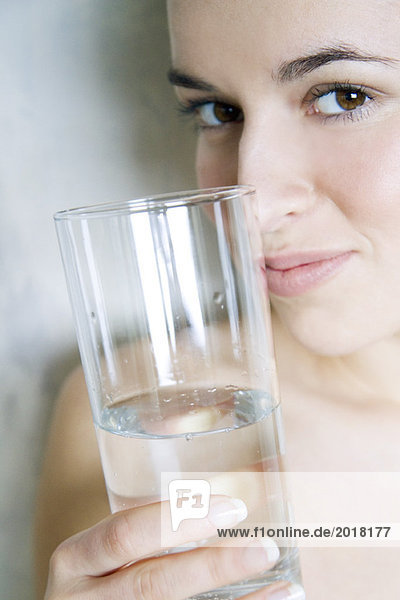 Junge Frau hält ein Glas Wasser  lächelt in die Kamera  Blick in den Ausschnitt