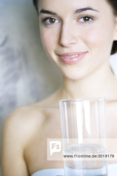 Junge Frau hält ein Glas Wasser und lächelt in die Kamera.