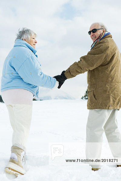Seniorenpaar geht zusammen  hält sich an den Händen  Mann schaut über die Schulter auf die Kamera
