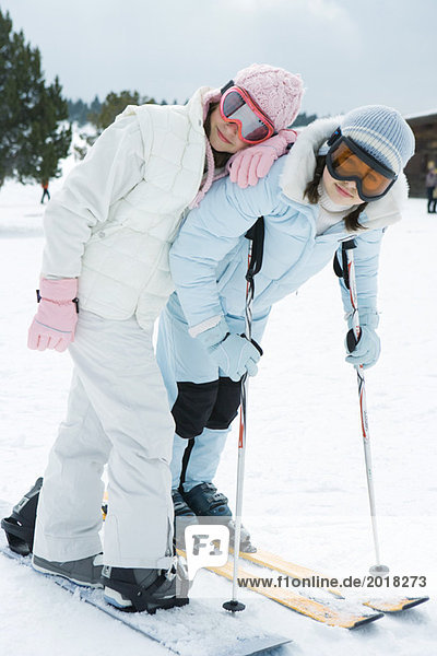 Two young skiers standing together  smiling at camera  one leaning on the other's shoulder  portrait