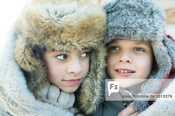 Sister and brother wearing fur caps  smiling  looking away  portrait