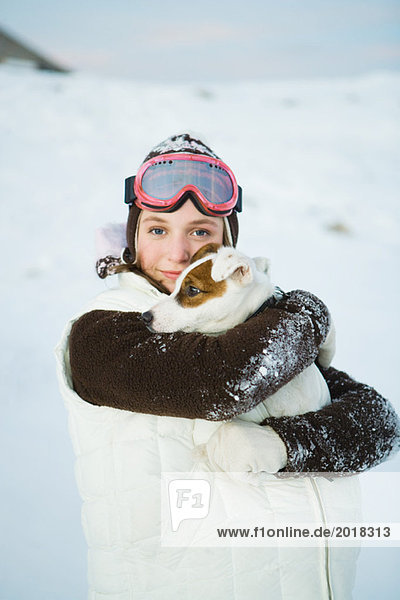 Teenagermädchen umarmt Hund  in Winterkleidung  lächelnd vor der Kamera  Portrait